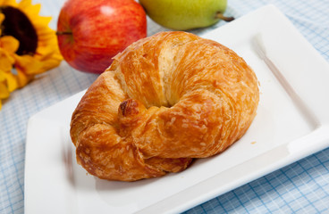 A croissant on a white plate with apples and sunflowers