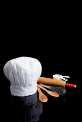 A chef's toque with kitchen utensils on black - obrazy, fototapety, plakaty
