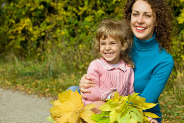 young woman and little girl laugh with leaves in hands in garden