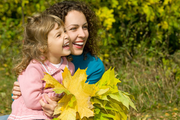 young woman and little girl laugh with leaves in hands in garden