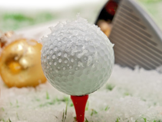 Golfball, Golfschläger und ein goldfarbener Weihnachtsball auf dem Schneebedeckten Gras