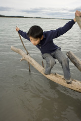 young Asian boy balancing on log in water