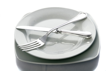 A white dinner plate with a fork and knife isolated
