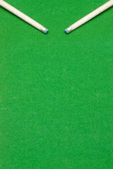Ends of two pool cue sticks against green baize texture