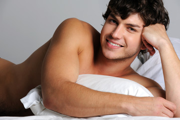 Handsome sexy smiling young man lying in bed