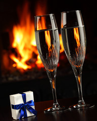 glasses with champagne and a gift, fire as the background