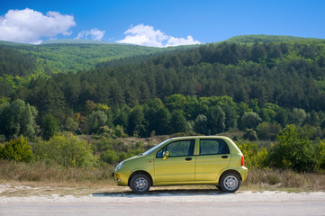 Obraz na płótnie Canvas Small olive green car against the background of mountain landsca
