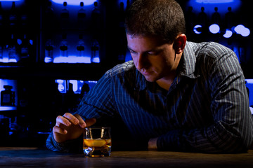 Worried man sitting at bar with whiskey glass. Dark night scene.