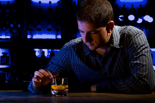 Worried Man Sitting At Bar With Whiskey Glass. Dark Night Scene.