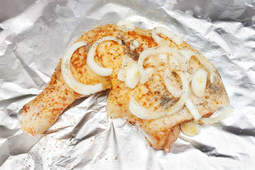 Raw chicken leg with pieces of fresh onion on aluminum foil