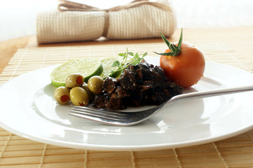 marinated cuttlefish with olive and tomato on a white plate