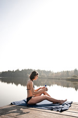 junge frau auf steg an see schützt sich mit sonnenmilch