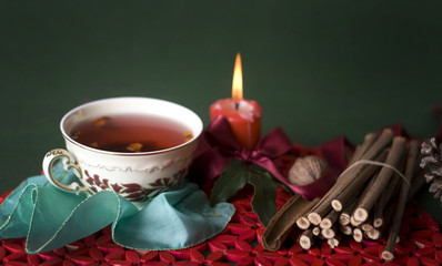 hot cup of tea with candle and sticks on green background