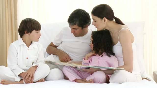 Parents reading with their children a book on bed