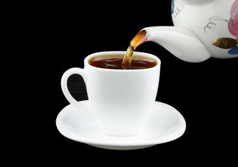 Pouring fresh tea to white cup isolated on black
