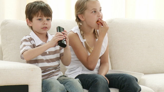 Children on sofa eating and watching television