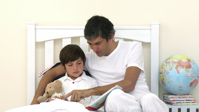 Father and son reading a book in bed