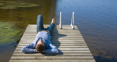 Northern summer - middle age man laying on an old wooden pier, s