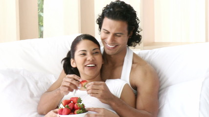 Panorama of couple sitting in bed eating strawberries - Powered by Adobe