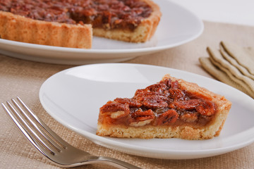 Slice of sweet delicious pecan pie with pie in the background