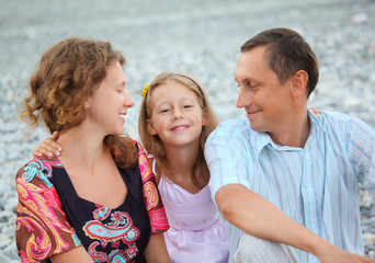 Happy family with girl sitting on beach, parents look on girl