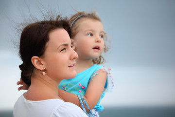 beautiful woman protects little girl from wind on seacoast