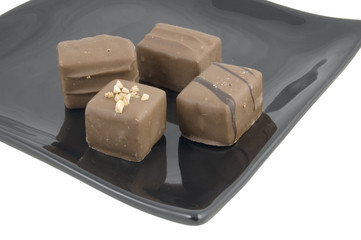 four square fancy chocolates on black plate on white