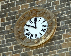 Reloj antiguo con numeros romanos en fachada de piedra.