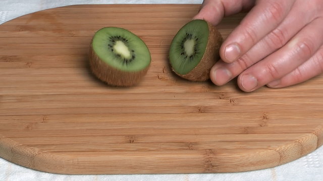 Kiwi cut by a kitchen knife on a chopping board.
