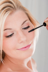 Young pretty woman applying mascara on her lashes