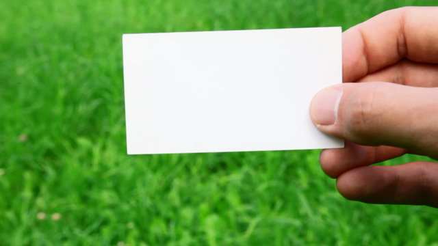 male hand holding business card on grass