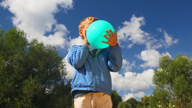 boy inflating blue balloon in park