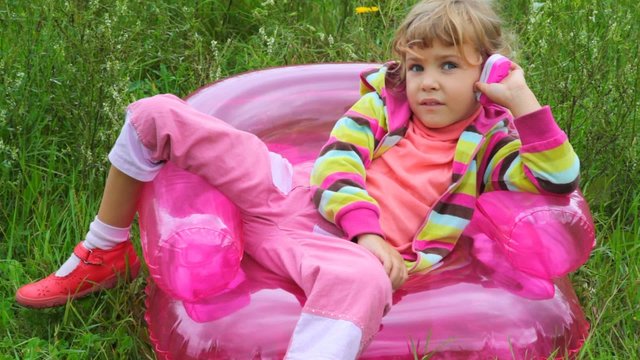 little girl with telephone sitting on inflatable armchair