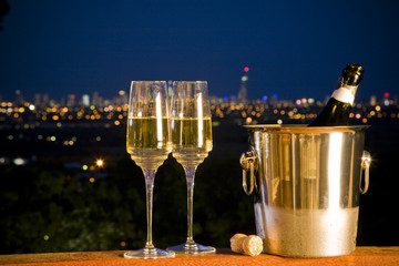 champagne bottle and two glasses with night skyline in backgroun