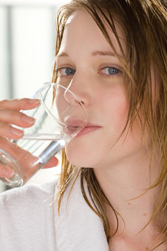 Frau im Bademantel trinkt ein Glas Wasser