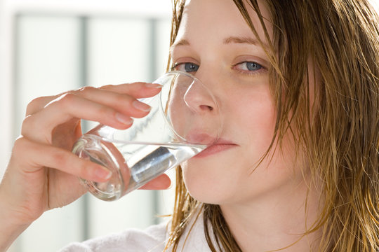 Frau im Bademantel trinkt ein Glas Wasser