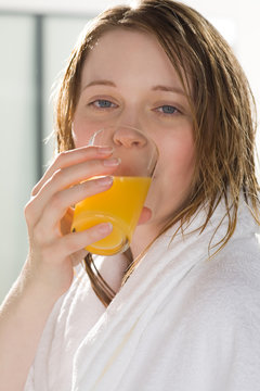 Frau im Bademantel trinkt ein Glas Orangensaft