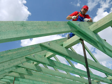 Carpenter driving a nail into house rafter framing beam