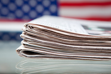 Stapel Zeitungen mit Flagge der USA dahinter auf Glastisch
