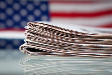 Stapel Zeitungen mit Flagge der USA dahinter auf Glastisch