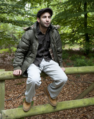 Naklejka na ściany i meble Man sitting on a fence in woodland.