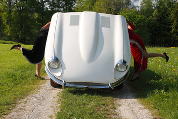 Frauen über Motor eines Oldtimers gebeugt.