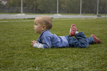 The little boy lies on the football field.
