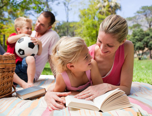 Mother and her daughter reading at a picnic with their family