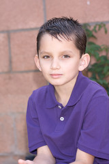 Portrait young biracial boy with short hair by brick wall