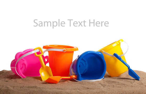 Assorted colored buckets on sand with copy space