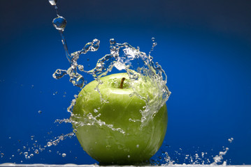 Fototapeta na wymiar Green apple with water splash on blue background