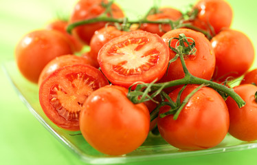 dojrzale czerwone pomidory na talerzu, na zielonym tle, grono - obrazy, fototapety, plakaty