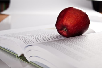 opened hefty book and fresh red apple