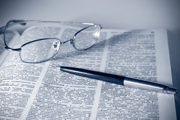 Open book, glasses and pen